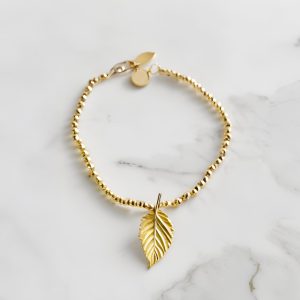 gold bracelet with gold leaf charm on a marble background