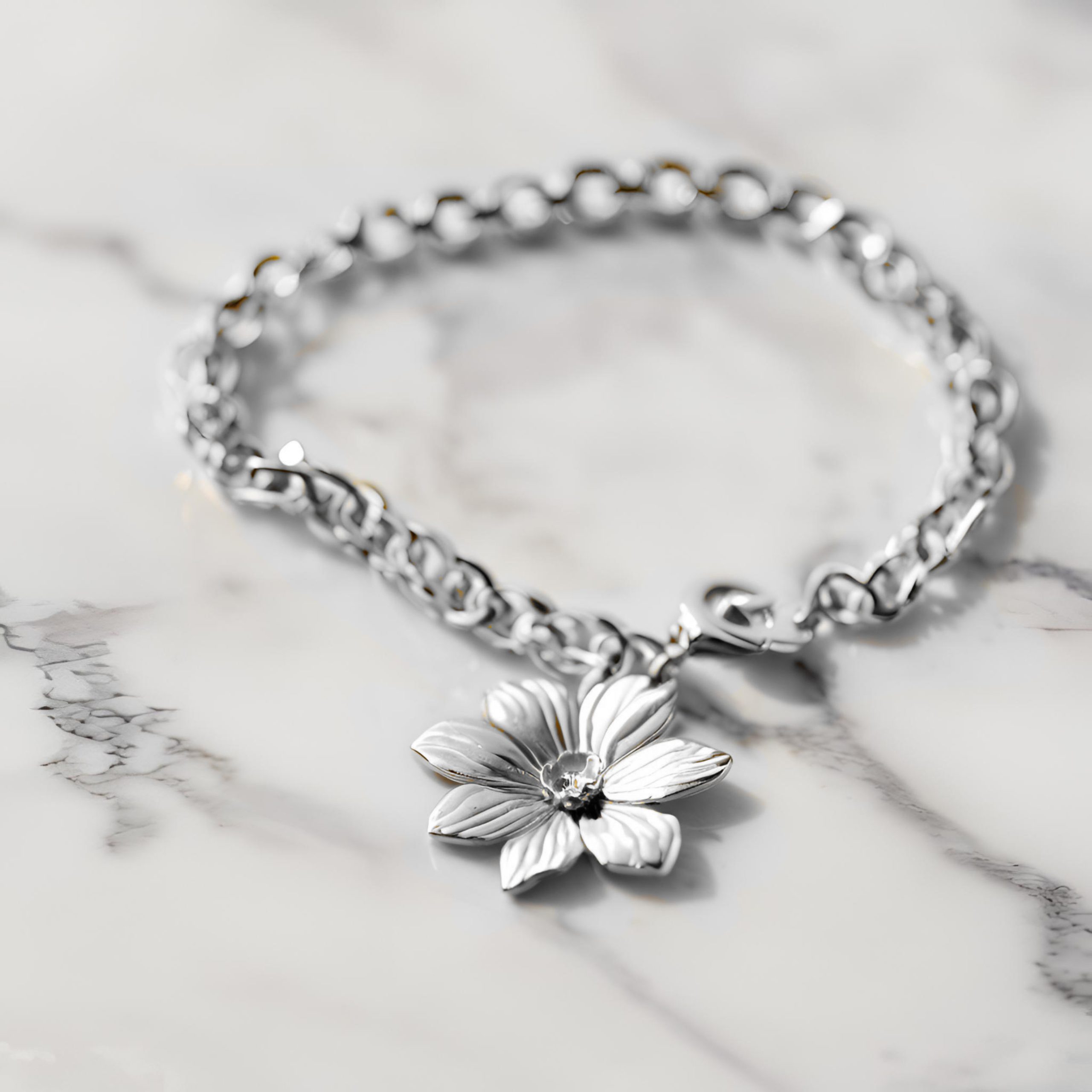 silver bracelet with silver flower charm on a marble background