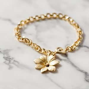 gold bracelet with gold flower charm on a marble background
