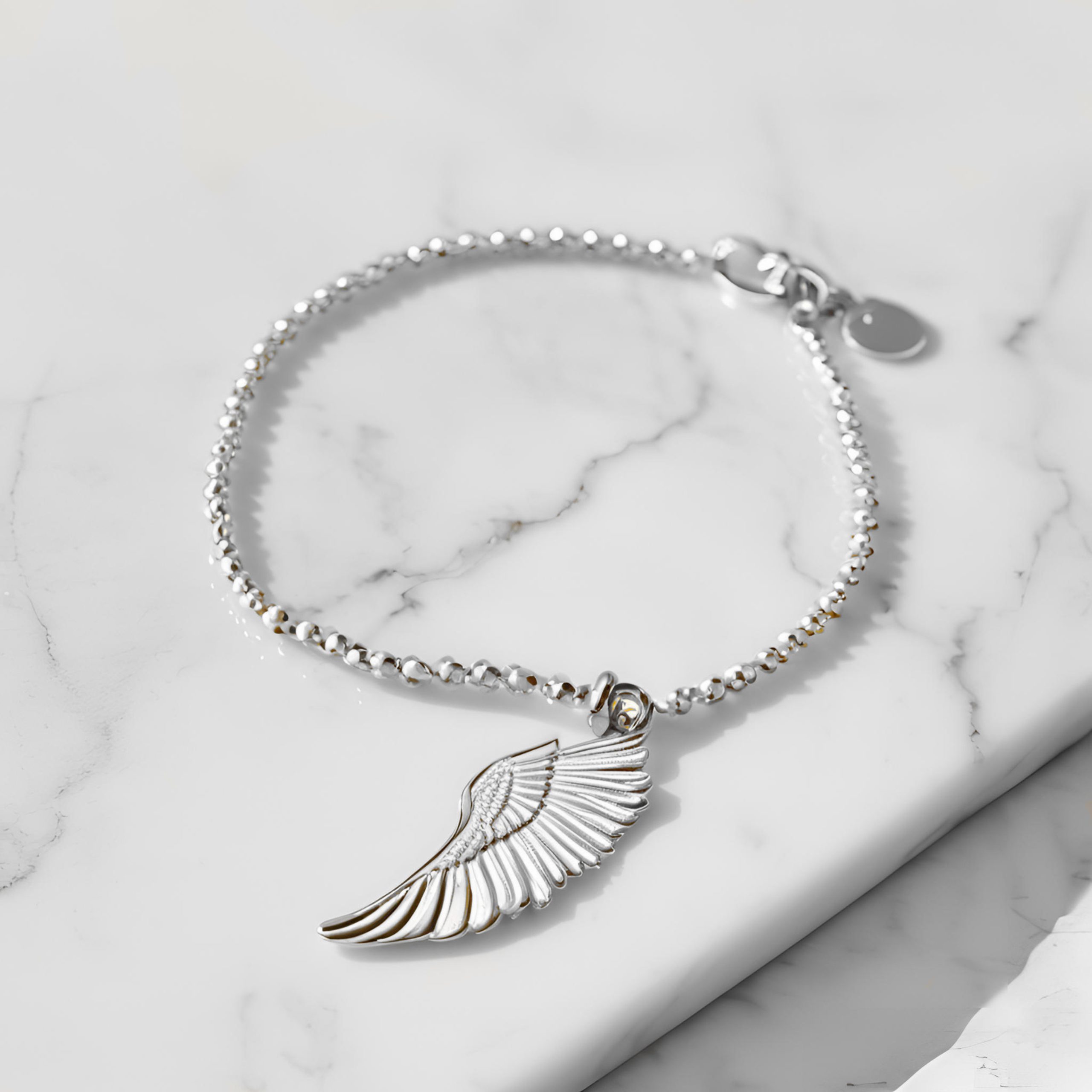 silver bracelet with silver wing charm on marble background
