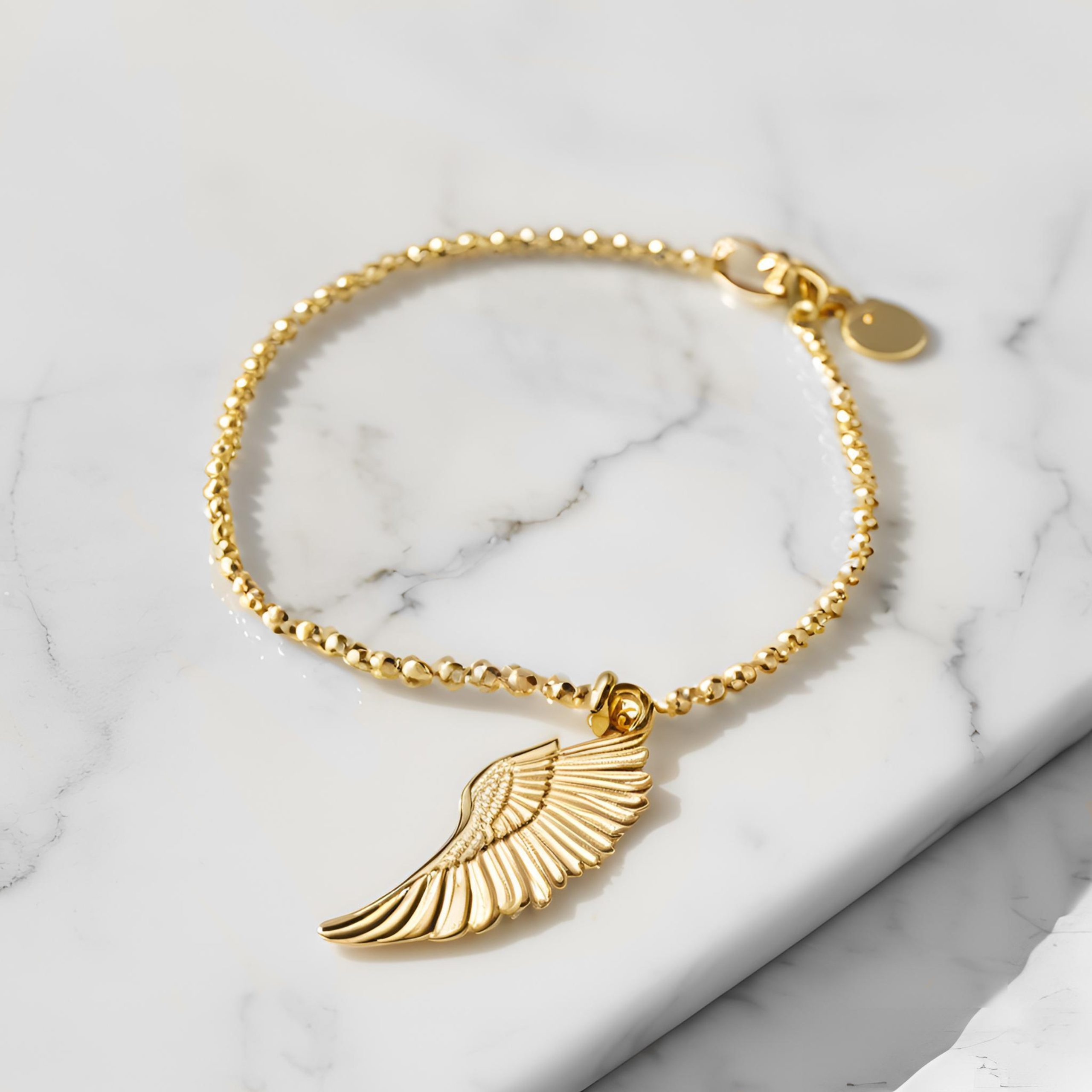 gold bracelet with gold wing charm on marble background
