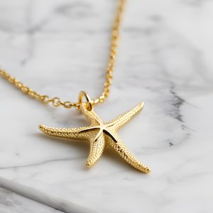 gold necklace with starfish gold charm on marble white background